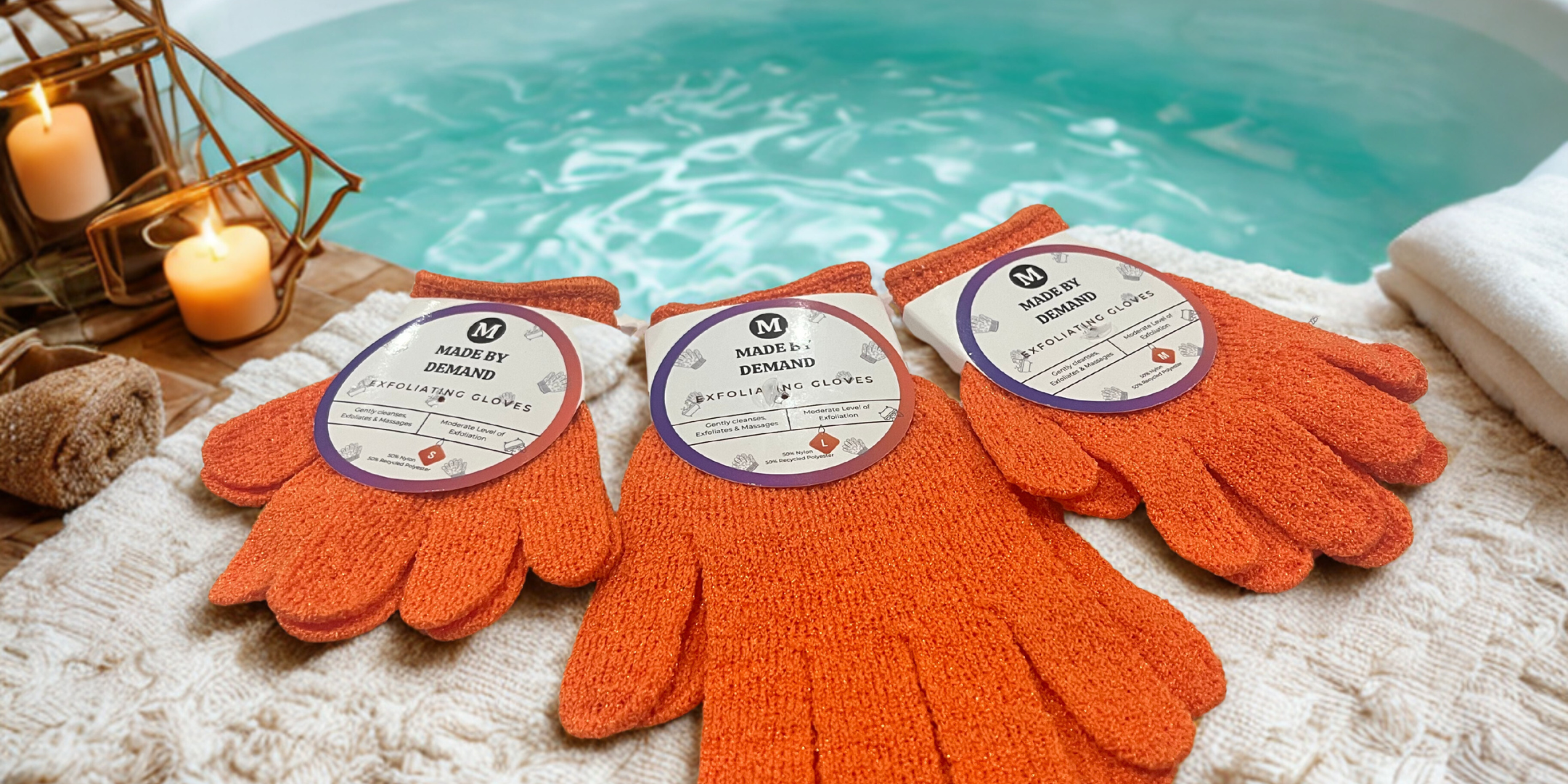 Three Made By Demand exfoliating orange gloves with labels on a textured surface near a pool.