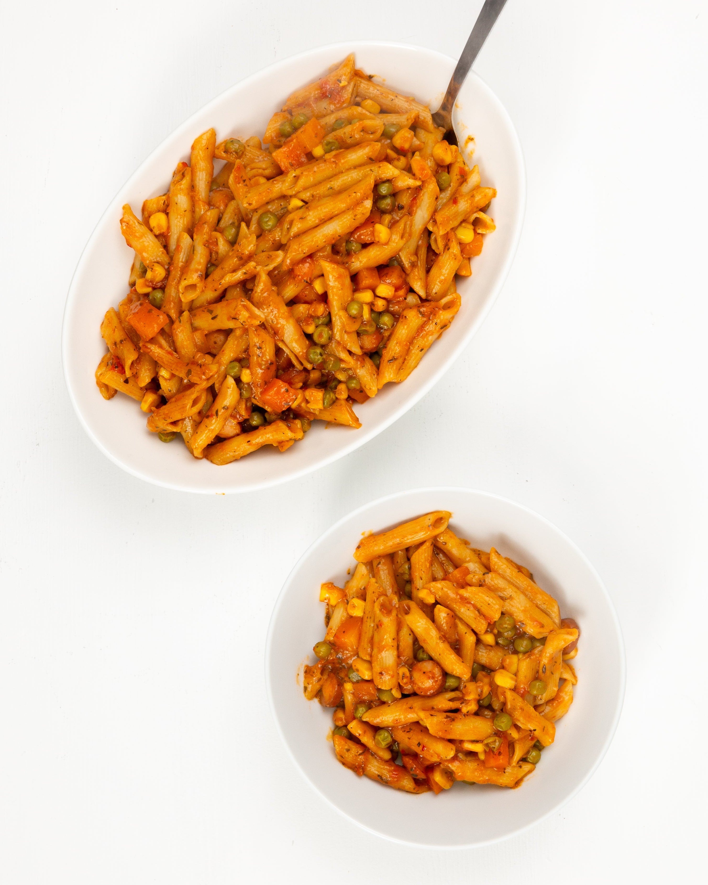 Two bowls of jollof pasta with a spoon on a white background
